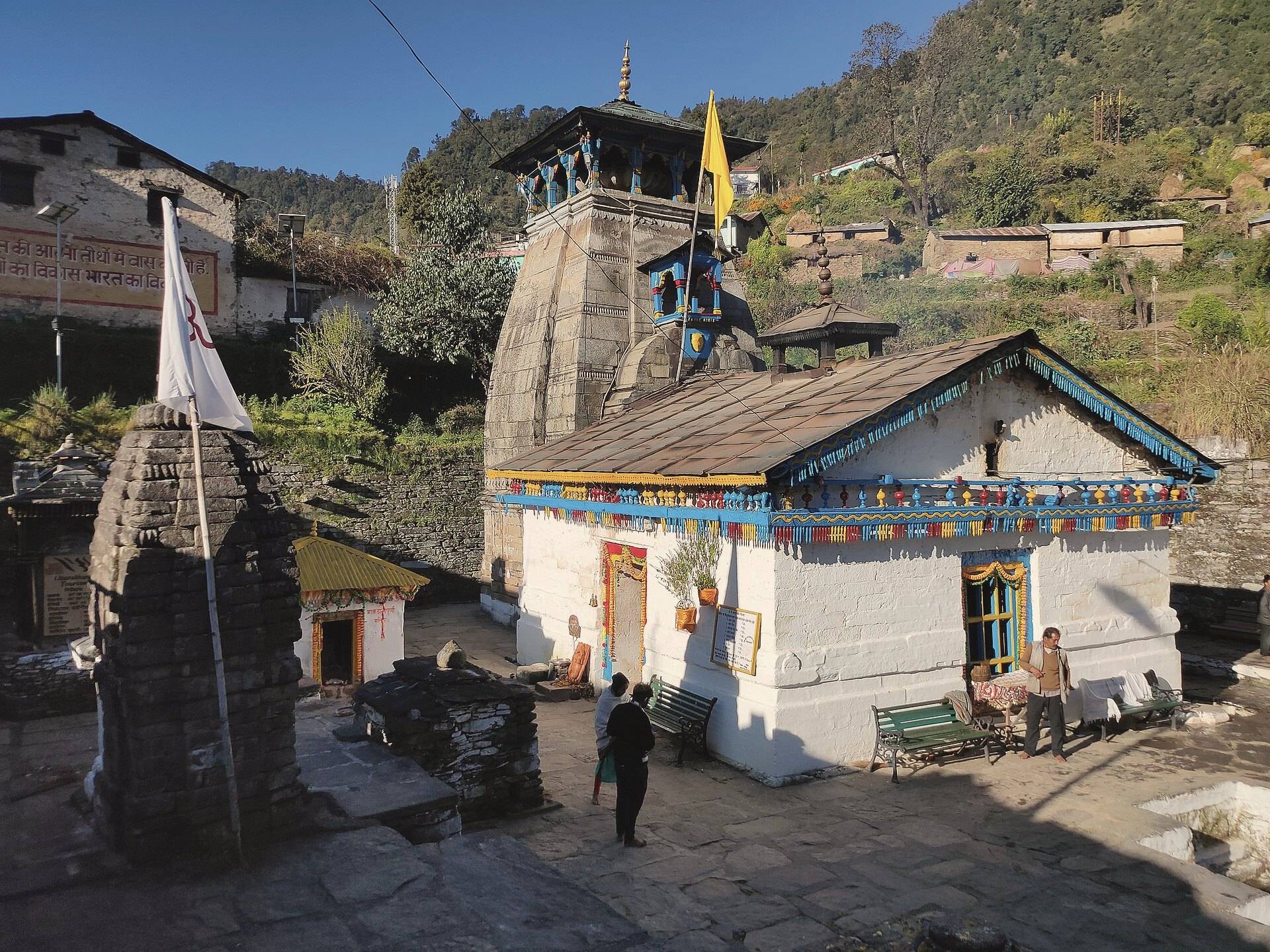 Triyuginarayan temple, a stone Himalayan shrine with a white hall and saffron flag, in the village square
