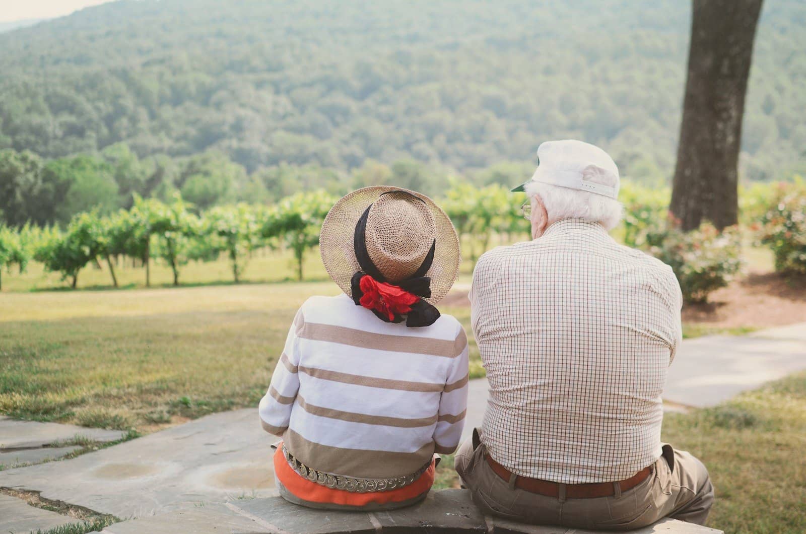 An older couple in sun hats sitting together looking at a green valley