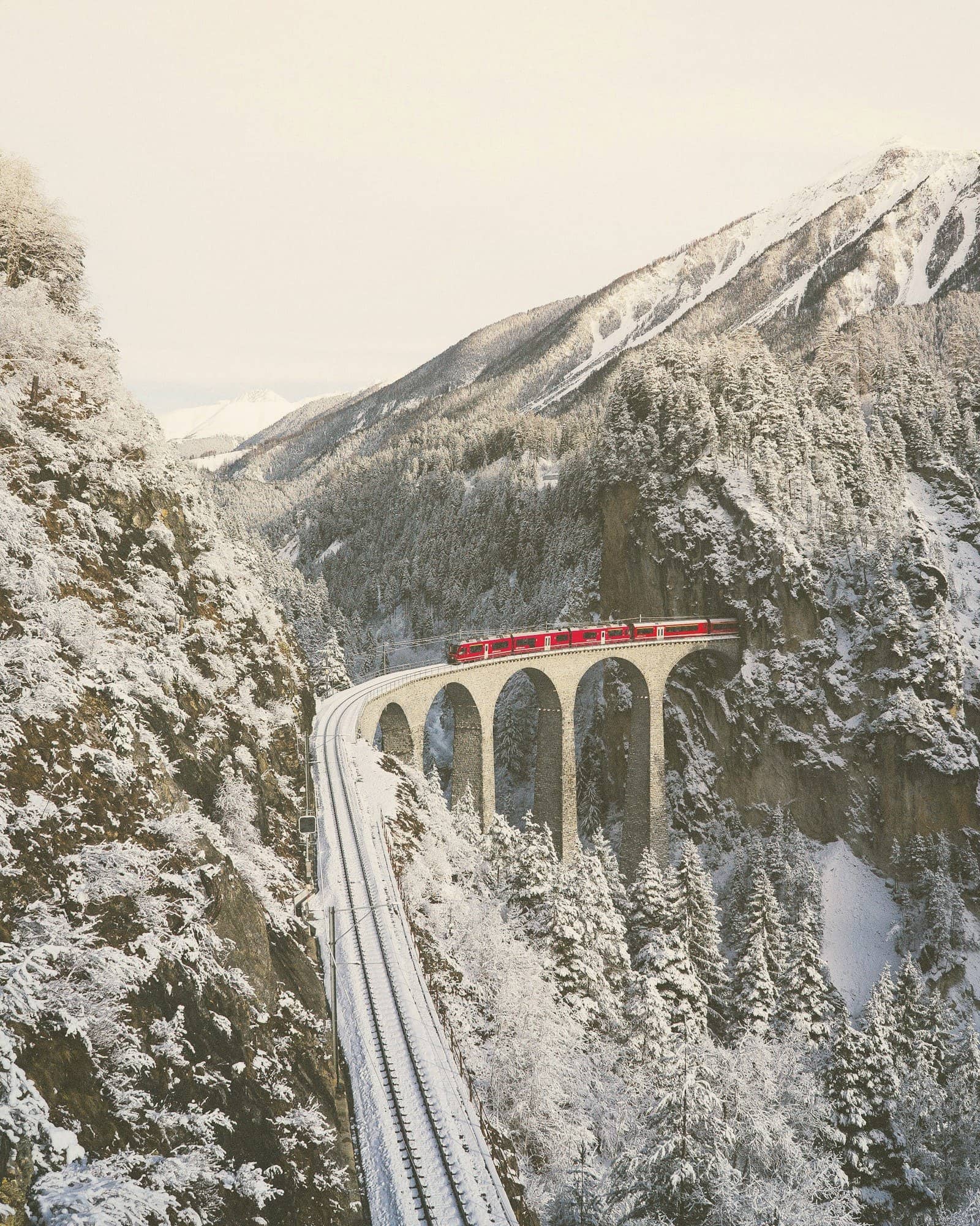 A red train crossing a stone viaduct through snowy Swiss mountains