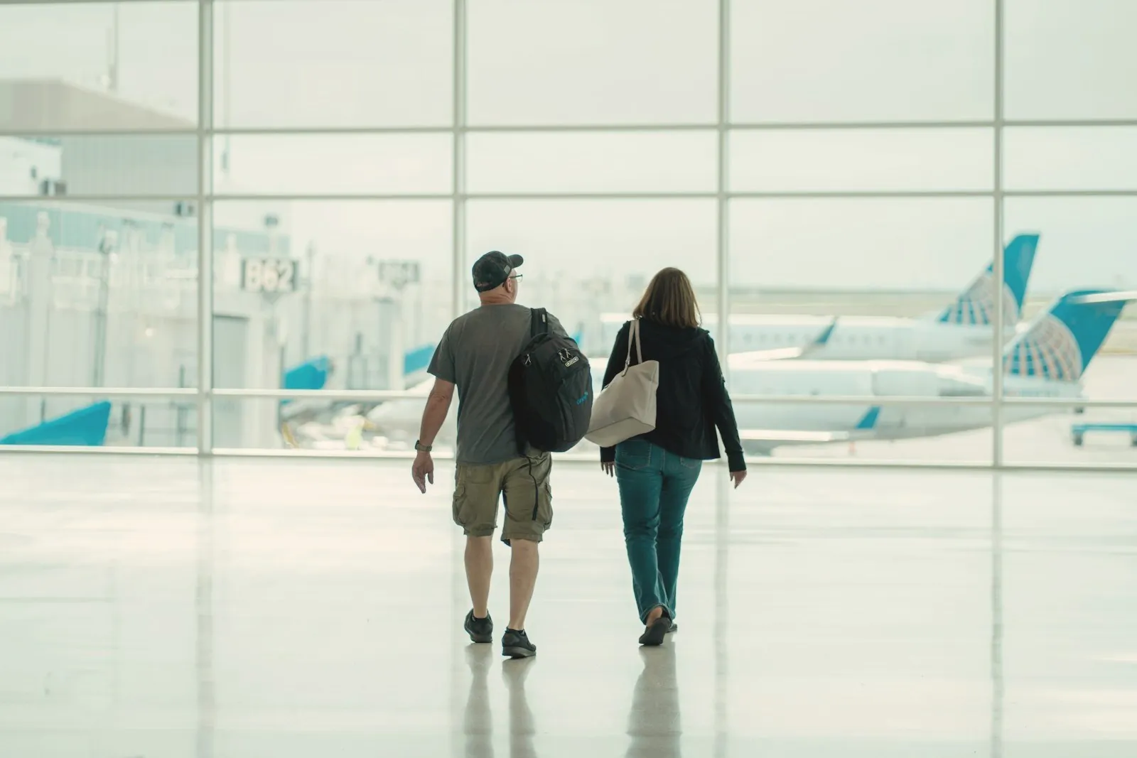 Two travellers walking through a bright airport terminal towards the planes